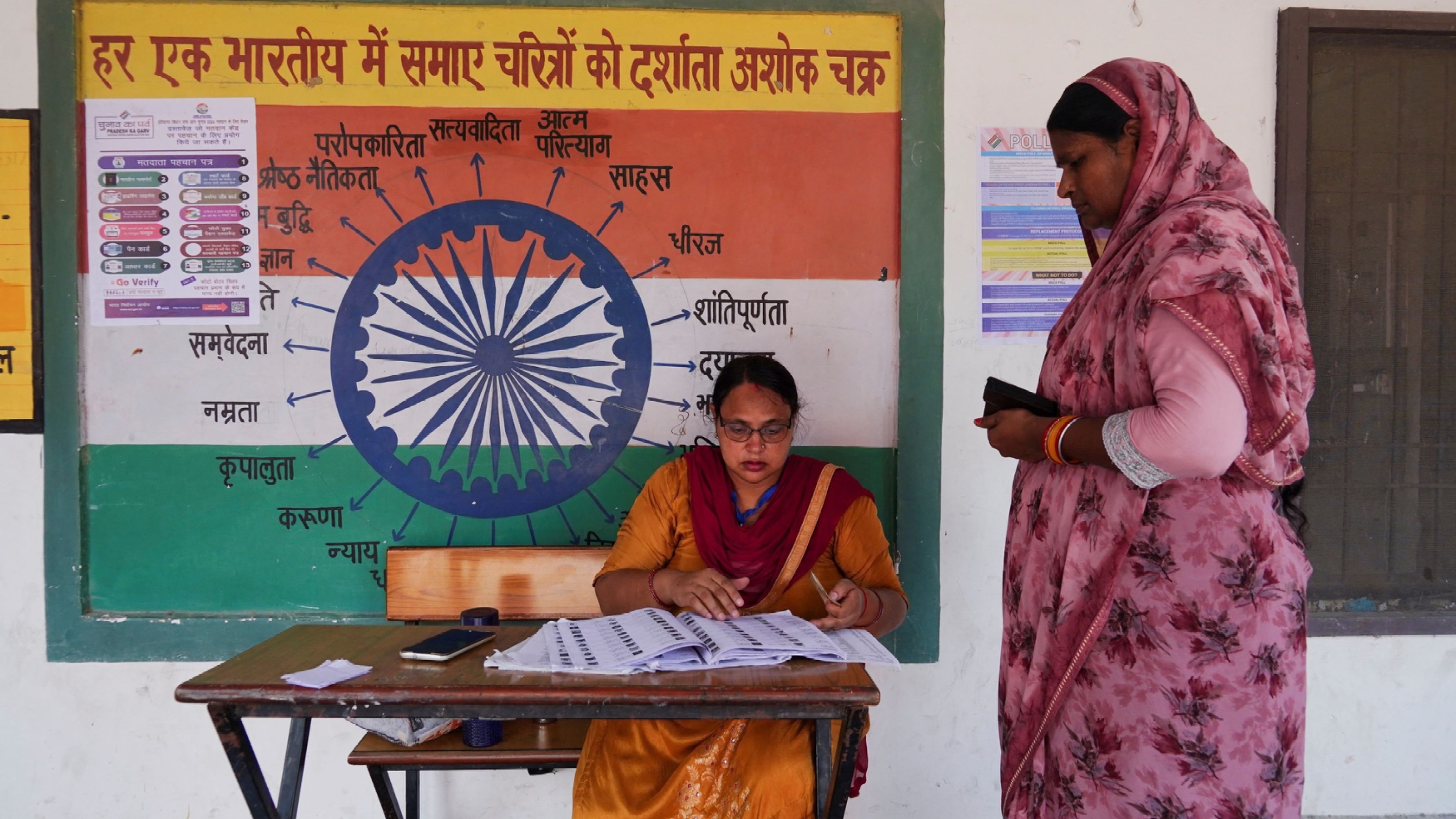 A booth-level officer helps a woman verify her name in the voting list outside a polling station. Representative purpose