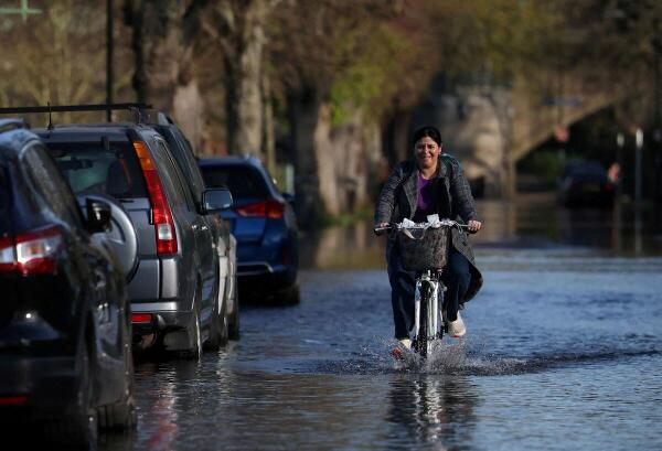A person cycles along a flooded road after the overtopping of the River Thames on a spring tide, in west London, Britain.