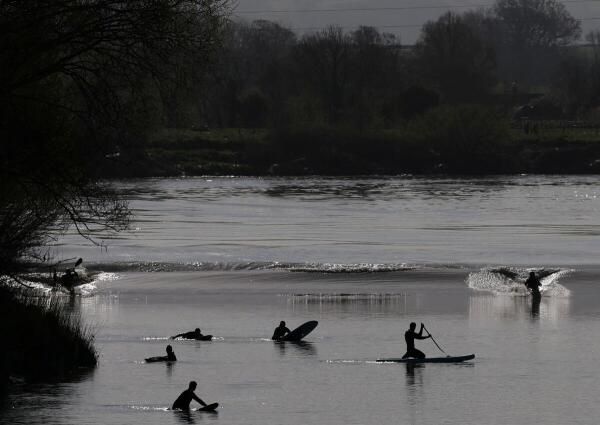 Surfers, kayakers and paddle boarders ride the Severn Bore surge wave, a natural phenomenon occurring according to the lunar cycle where a set of waves push through the Severn River estuary and upstream on a high tide, on the only day in 2025 where it is given a four star size status, at Minsterworth, near Gloucester in Britain.