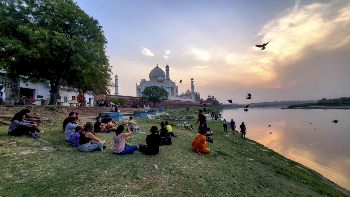 Foreign tourists sit on the bank of Yamuna river near the Taj Mahal during sunset, in Agra