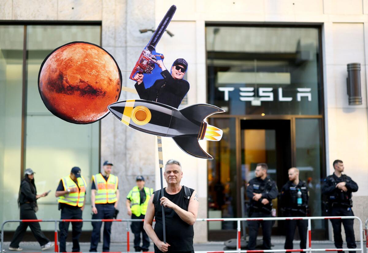  man holds a cutout of Elon Musk during a protest by activists of the "New Generation" (Neue Generation) and Extinction Rebellion in front of a Tesla store in Berlin, Germany April 30, 2025.