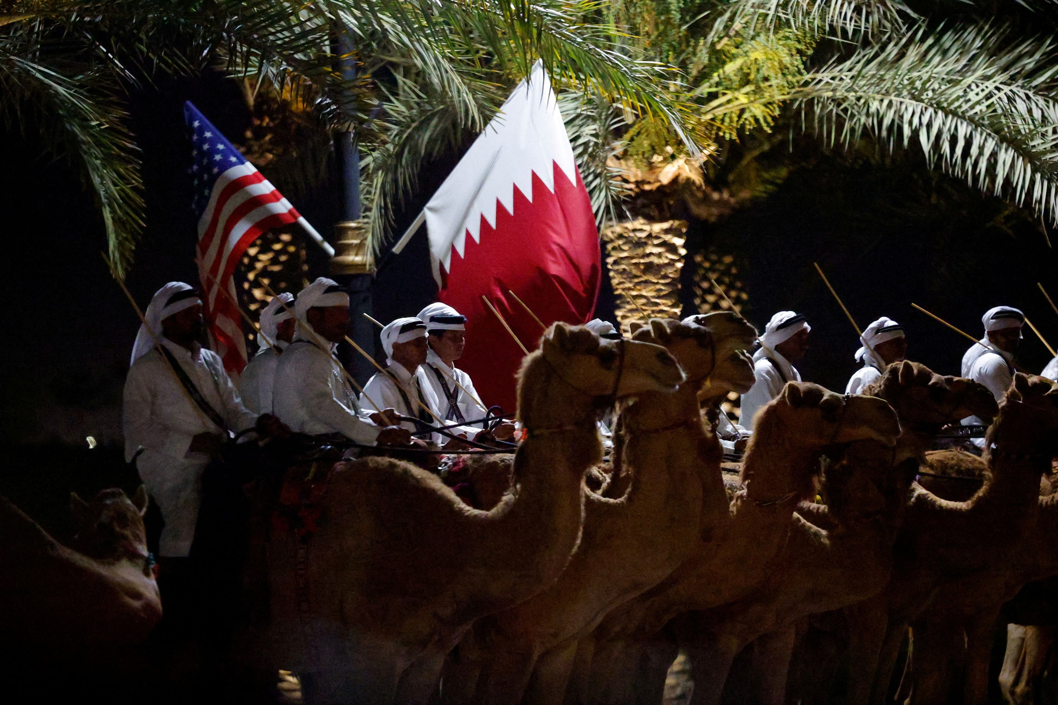 Members of an honour guard sit on camels next to U.S. and Qatari flags ahead of a state dinner at Lusail Palace hosted by Qatar's Emir Tamim bin Hamad Al Thani during a visit by U.S. President Donald Trump, in Lusail, Qatar