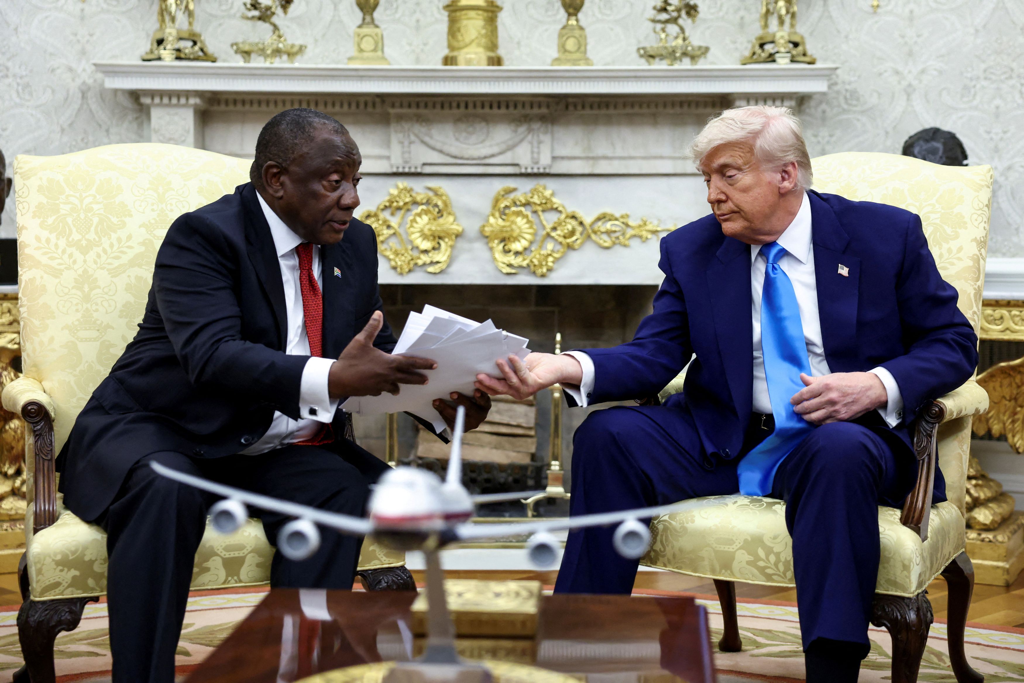 U.S. President Donald Trump hands over to South African President Cyril Ramaphosa copies of articles that he said showed white South Africans who had been killed, in the Oval Office of the White House in Washington, D.C., U.S., May 21, 2025. 