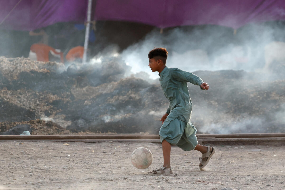 A boy plays with a soccer ball next to a smouldering pile of rubbish, on World Environment Day, in Karachi, Pakistan