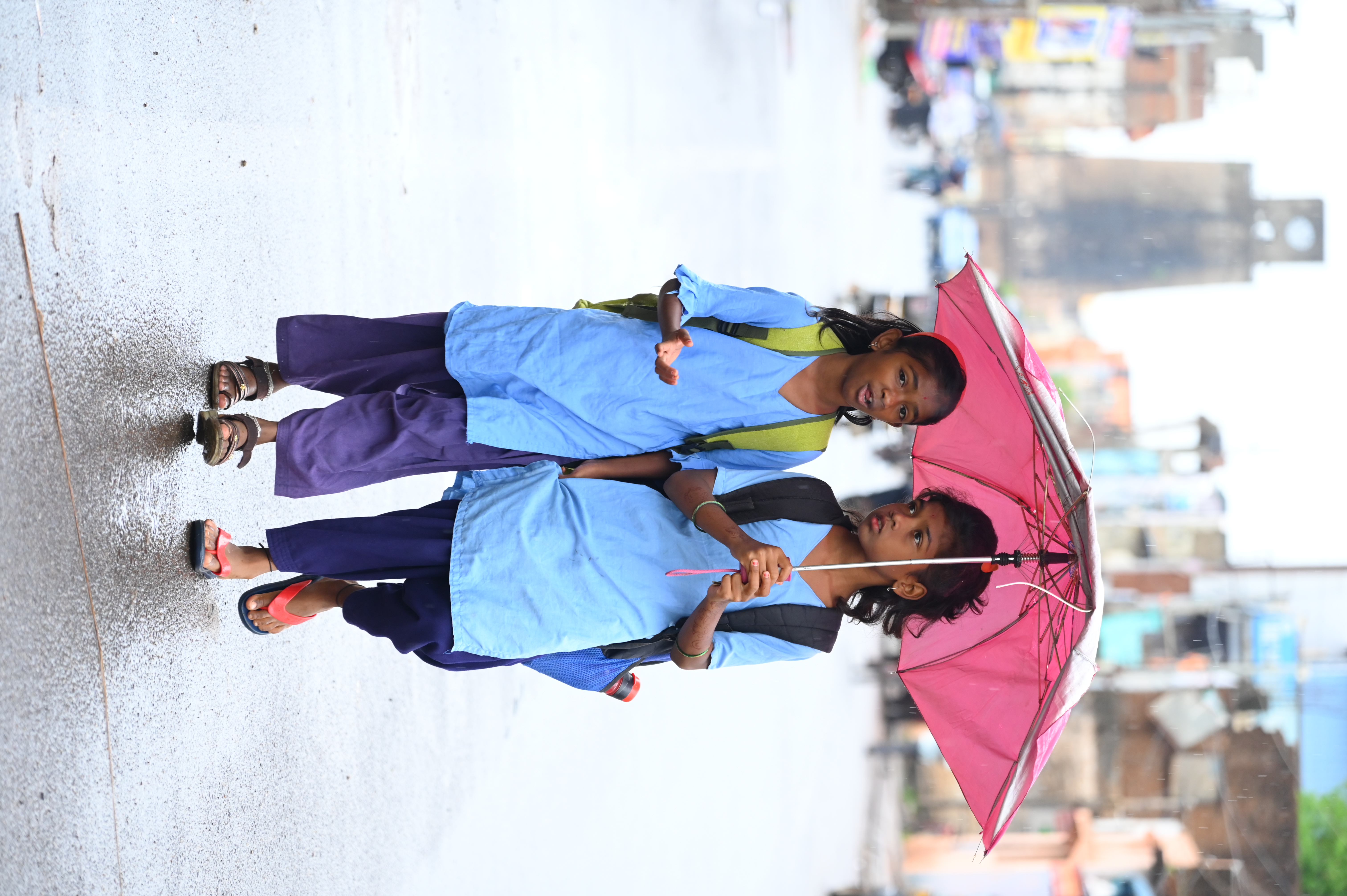 Students take shelter from rain under an umbrella on their way to school near Chowbara in Bidar on Monday.