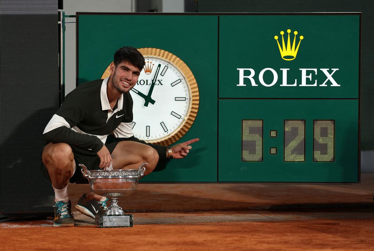 Spain's Carlos Alcaraz poses with the trophy as he points to the clock after playing the longest ever men's singles final at Roland Garros in history.