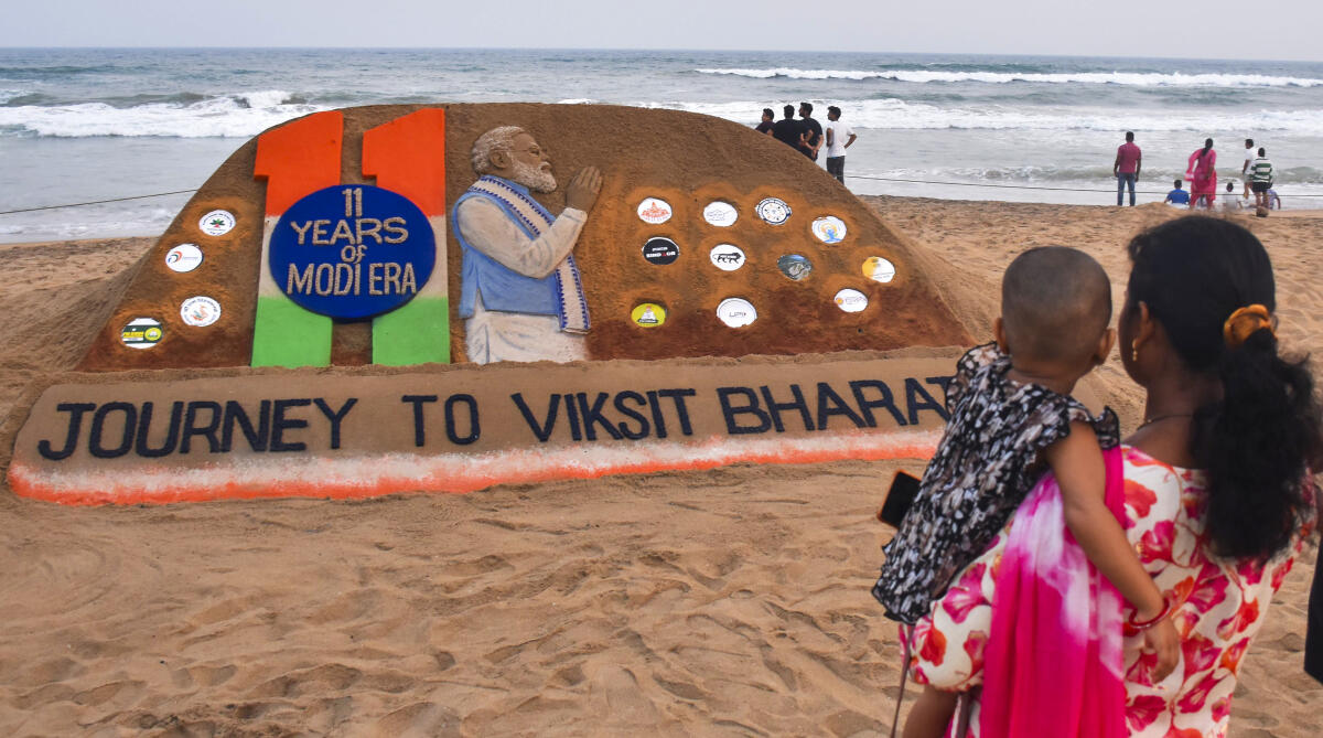 Visitors look at a sand sculpture created by sand artist Sudarsan Pattnaik celebrating Prime Minister Narendra Modi's 11 years in office, at Puri beach, in Odisha, Sunday, June 8, 2025.