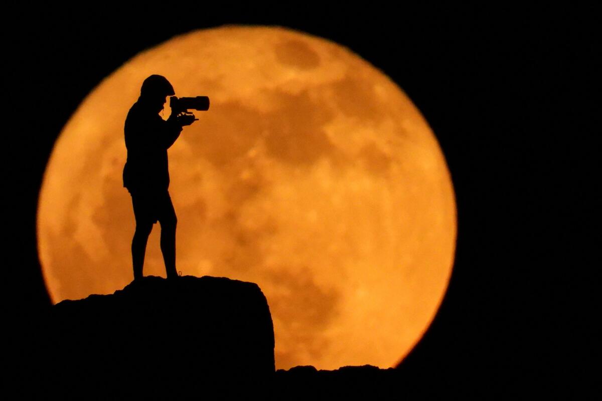 A photographer is silhouetted against the full moon known as the strawberry moon in Arinaga, on the island of Gran Canaria, Spain, June 11, 2025.