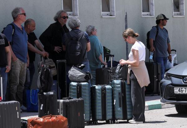 Expats, including diplomats from different nationalities, who were stranded in West Bank and Israel, wait as they hold belongings while being evacuated through the King Hussein Bridge crossing, in South Shuna