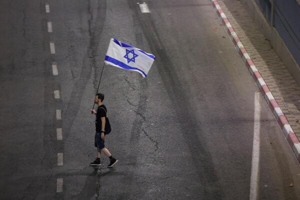 A demonstrator walks on a road with an Israeli flag, during a protest to demand the immediate release of hostages held in Gaza since the October 7, 2023 attack on Israel by Hamas