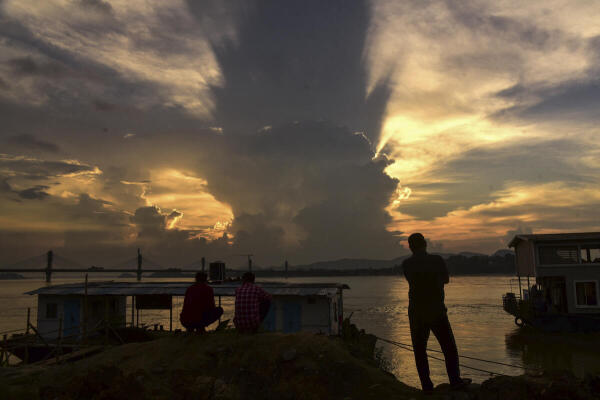 People get silhouetted against the setting sun on the banks of the Brahmaputra river, in Guwahati