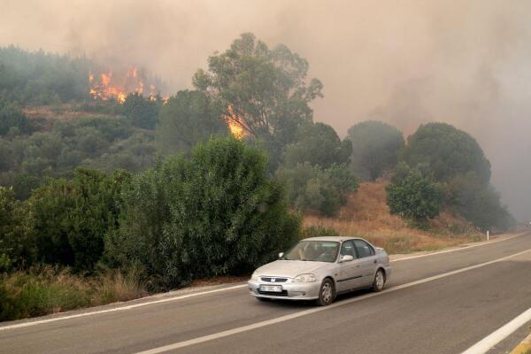 A car drives past as a wildfire burns near Seferihisar in Izmir province, Turkey