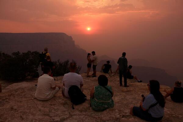Smoke from the Dragon Bravo Fire colors a setting sun for onlookers at Grandeur Point on the southern rim of Grand Canyon, Arizona, US.