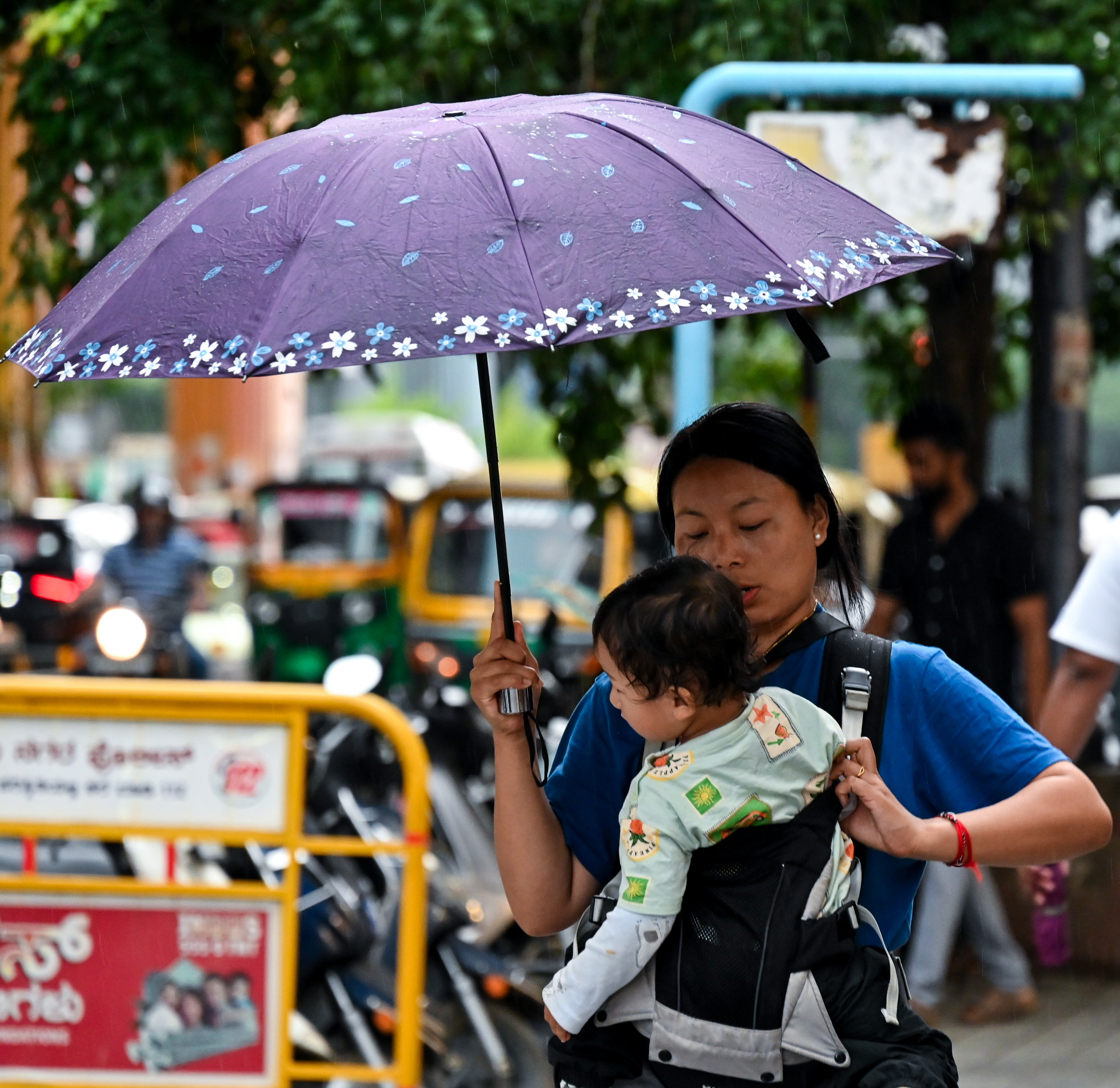 A woman along with her child take cover under an umbrella during sudden showers on Sunday. DH PHOTO/PUSHKAR V