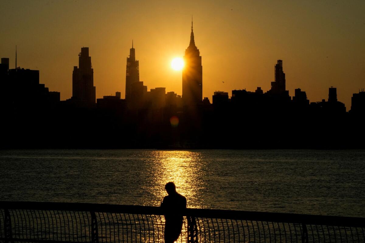 The sun rises behind the Empire State Building and the New York City skyline as a person stands along the riverfront amid an extreme heat warning, in Hoboken, New Jersey