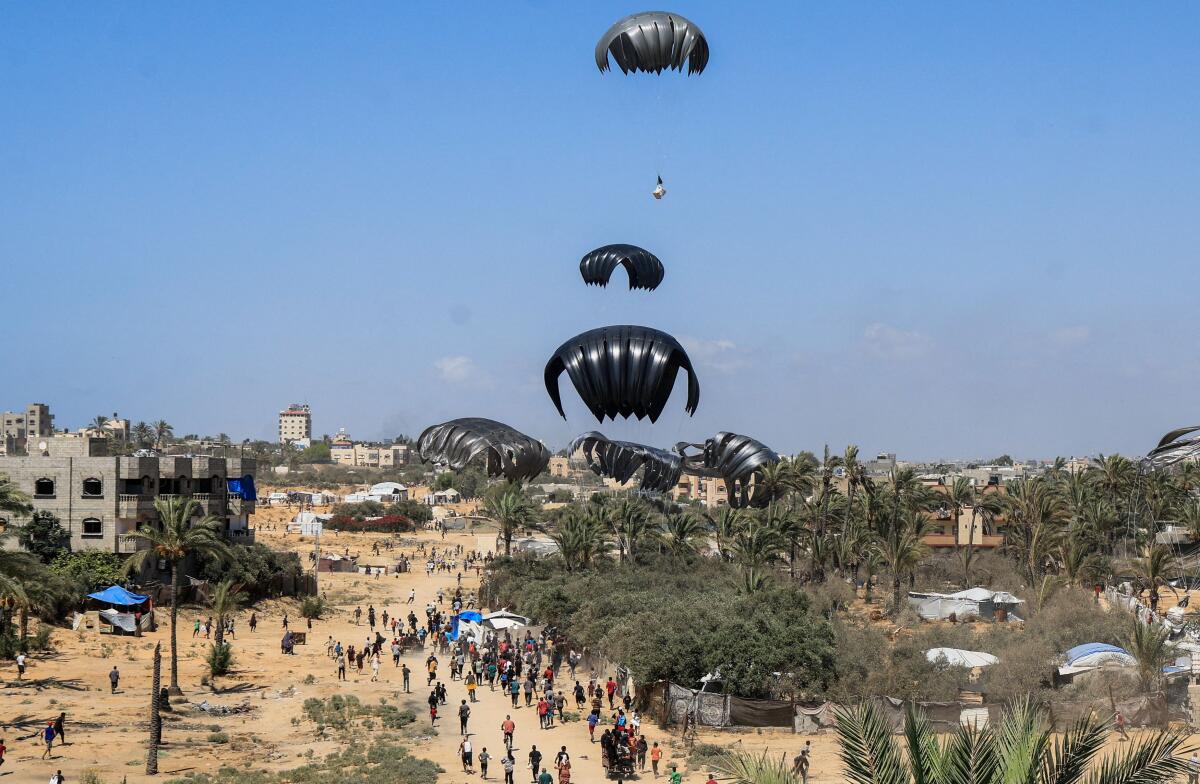 Aid packages, dropped from an airplane, descend over Gaza, as seen from the central Gaza Strip, July 31, 2025. 