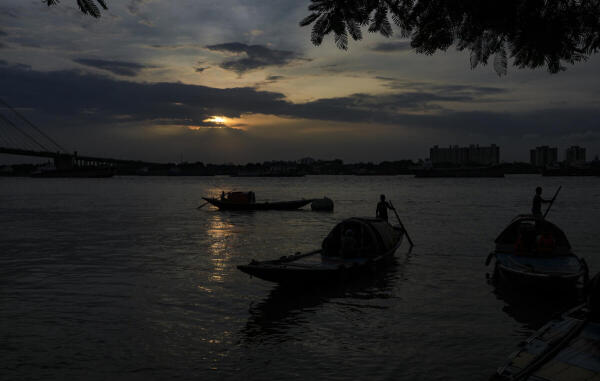 Boatmen row their boats in the Hooghly river near Prinsep Ghat as the sun sets behind clouds, in Kolkata, West Bengal.