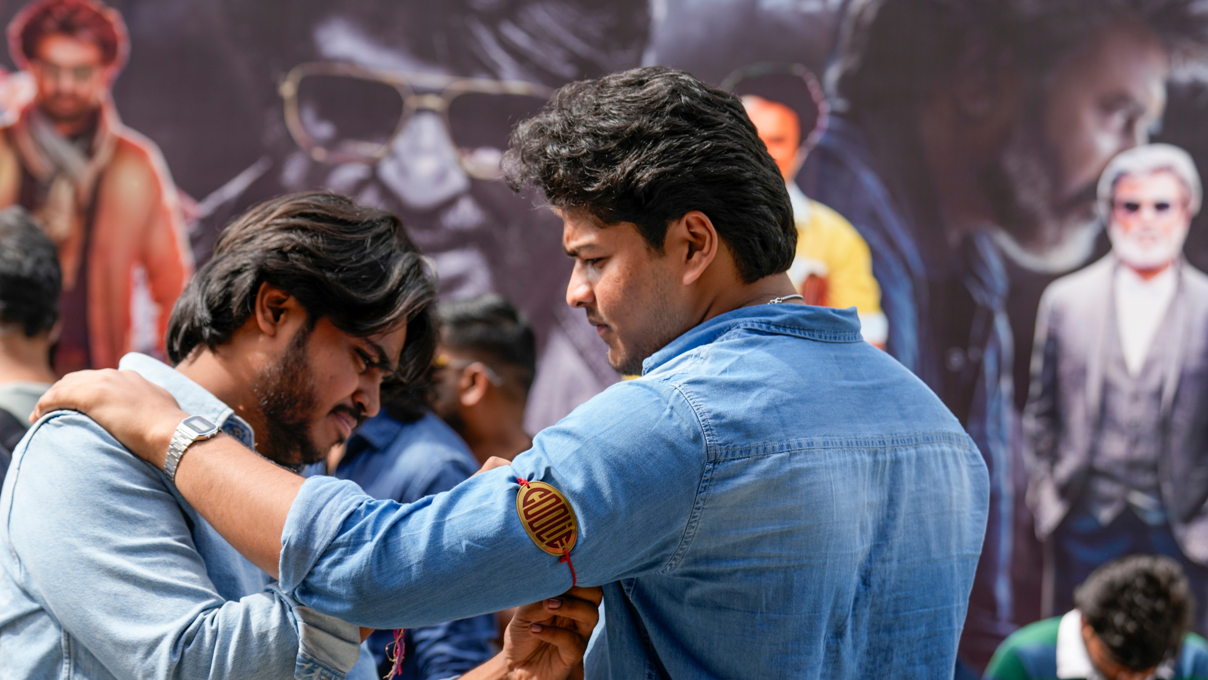A Rajinikanth fan ties an armband on a fellow supporter as part of the celebrations for the release of Coolie, outside a cinema in Chennai.