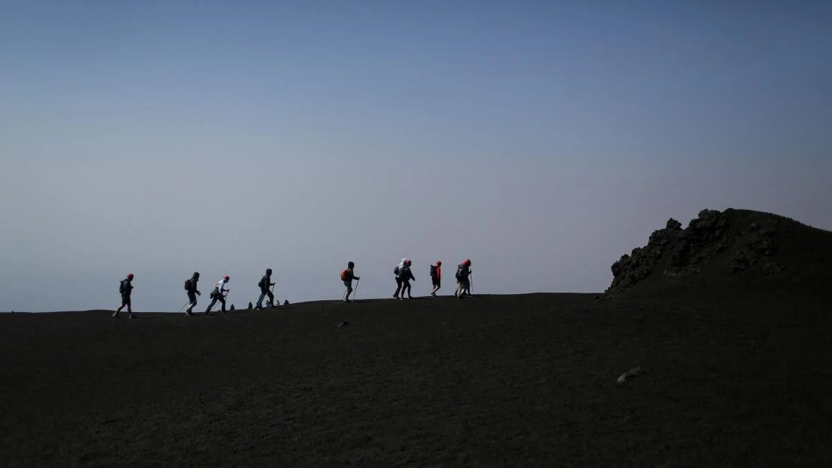 Tourists form a line while hiking along a ridge of Mount Etna in Catania, Sicily, Italy.