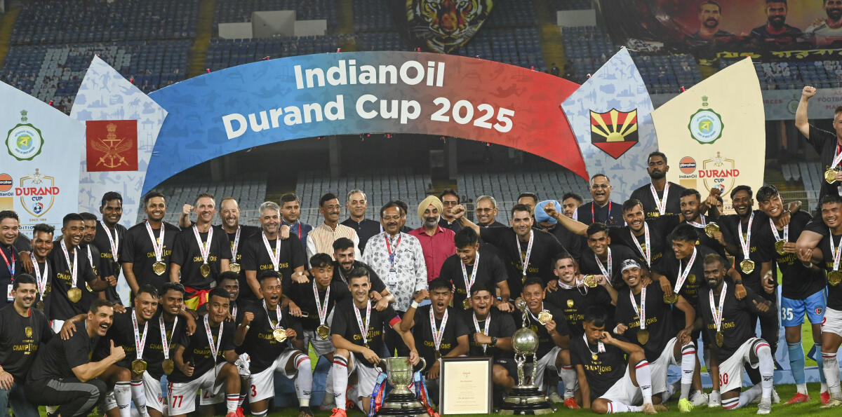 NorthEast United FC's players, along with Union Minister of State for Defence Sanjay Seth, West Bengal Sports Minister Aroop Biswas and Chief of the Air Staff Air Chief Marshal Amar Preet Singh, pose with the trophy after winning the Durand Cup 2025, at Vivekananda Yuba Bharati Krirangan, in Kolkata, Saturday, Aug. 23, 2025.