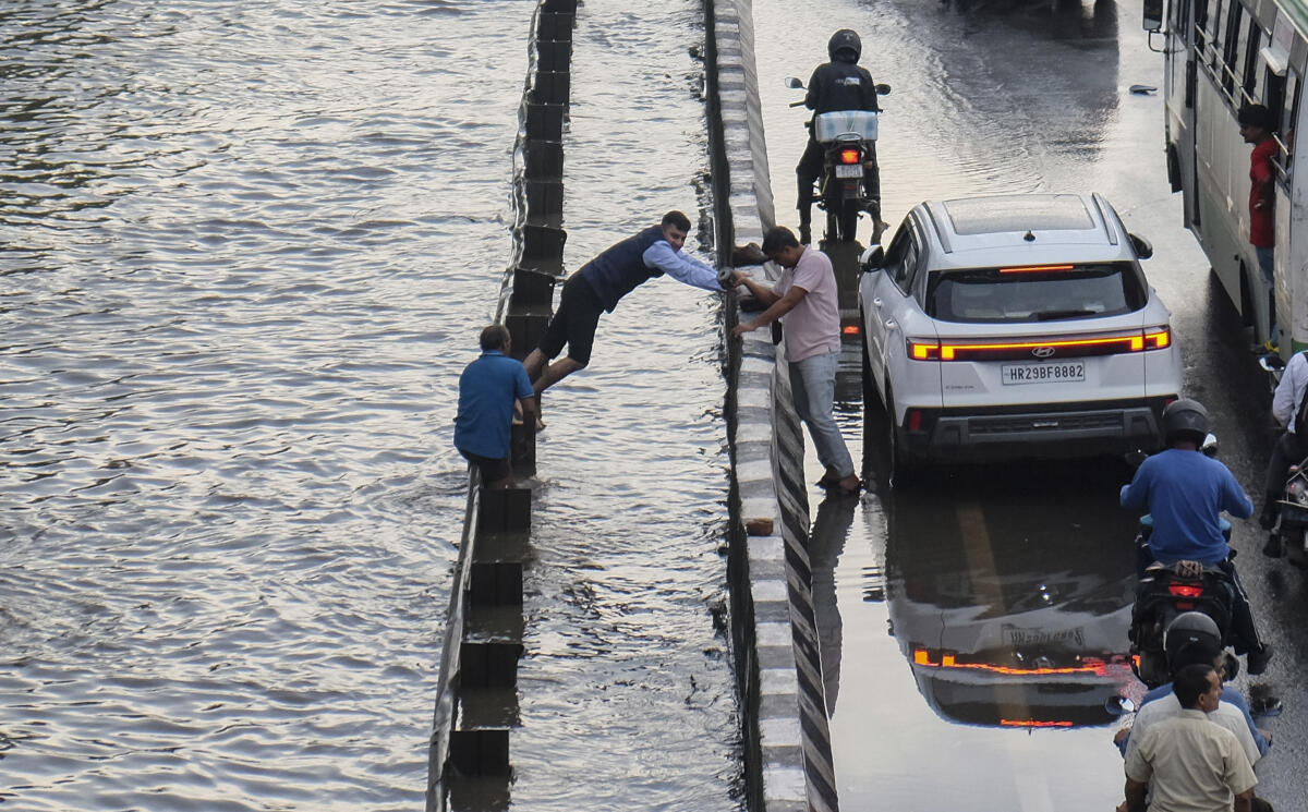 A man tries to cross a waterlogged divider following heavy rainfall, at the Delhi-Gurugram Expressway, Tuesday, Aug. 26, 2025.