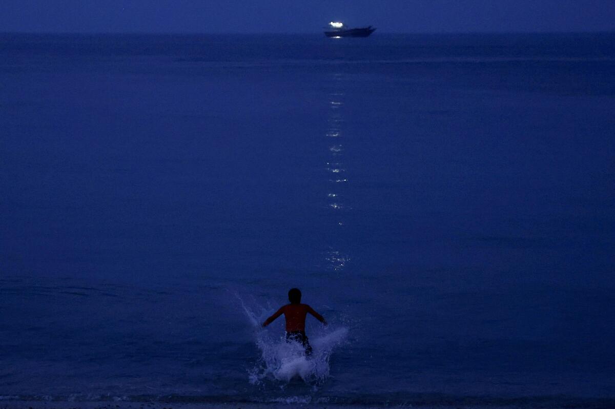 Water splashes as a boy jumps in for a swim, with a sailing ship visible in the background, in Musandam, Oman, August 25, 2025.