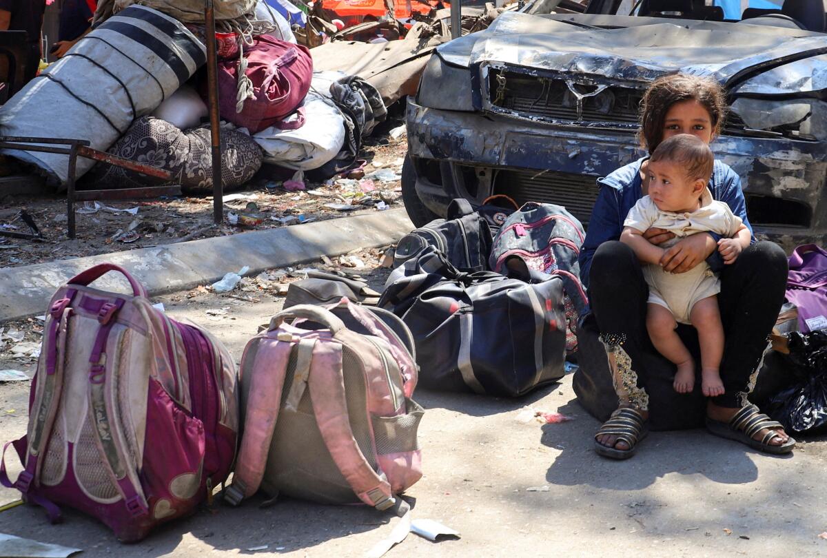 A Palestinian girl holds a child next to belongings laying on the ground, as displaced Palestinians flee amid an Israeli military operation, in Gaza City, August 26, 2025.