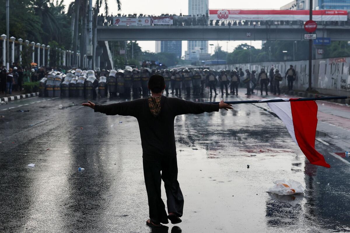 A demonstrator carrying an Indonesian flag gestures to riot police during a clash at a protest against what the demonstrators say are exorbitant allowances for Indonesian parliament members, outside Indonesian parliament buildings in Jakarta, Indonesia