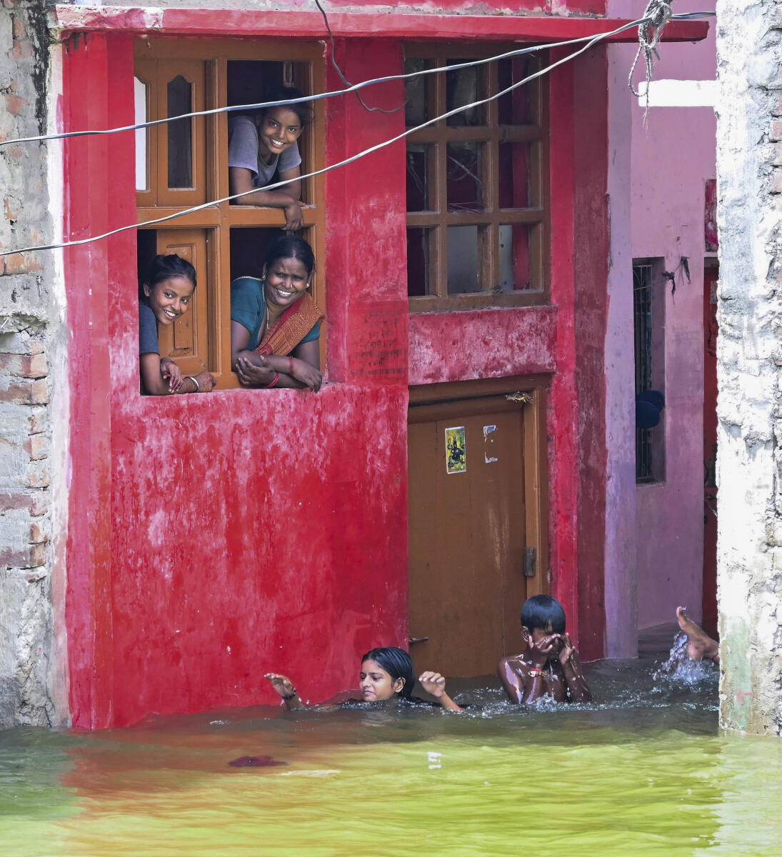 People look out from windows as children take a dip in the swollen Ganga river and its tributaries inundating an area, in Varanasi, Uttar Pradesh