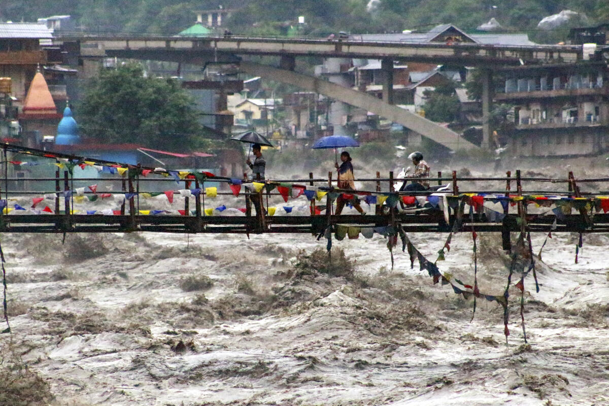 People walk along the bridge over the swollen Beas river amid rainfall, in Kullu district, Himachal Pradesh.