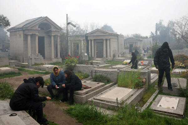 Demonstrators sit on graves inside the General Cemetery after fleeing clashes with police outside, during a rally ahead of the 52nd anniversary of Chile's 1973 military coup, in Santiago, Chile.