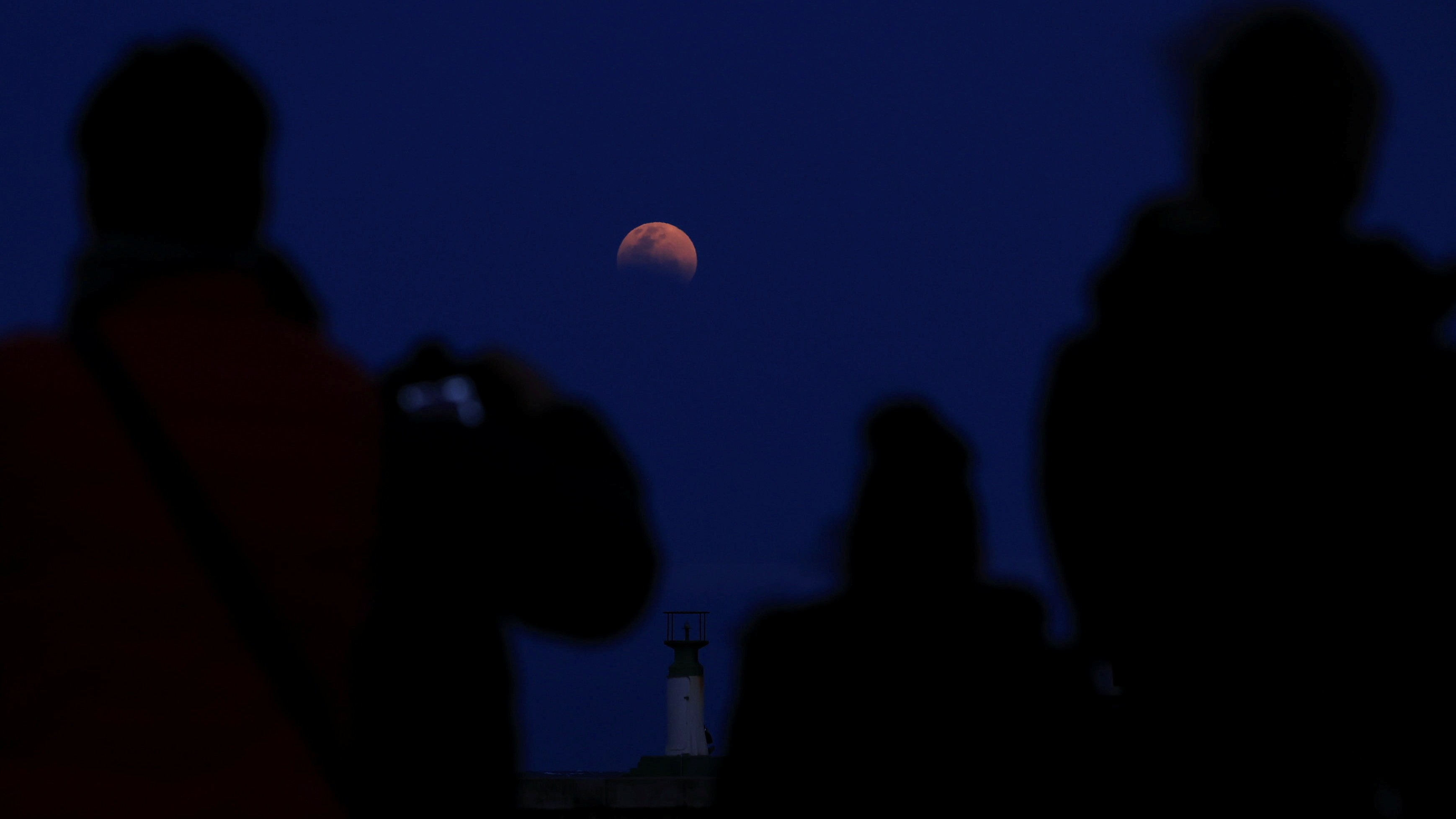 People gather to watch the 'Blood Moon' rising over Kalk Bay harbour on the night of a total lunar eclipse in Cape Town, South Africa.