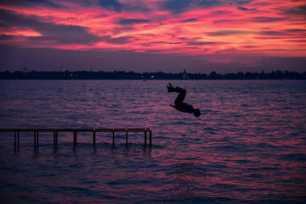 A youth dives into the swollen river Ganga during dusk, in Prayagraj, Uttar Pradesh.