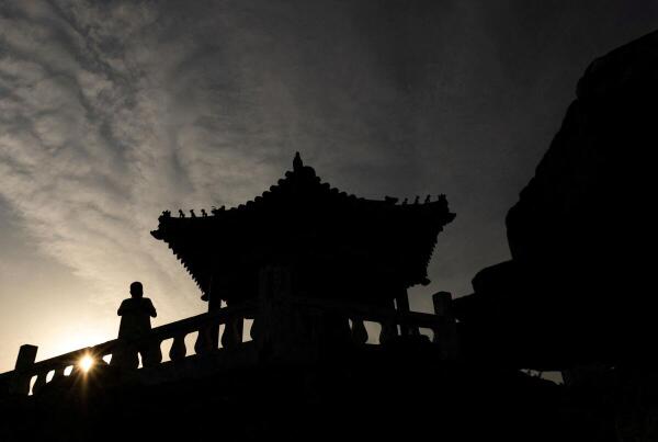 A man stands next to a traditional Chinese pavilion in Ritan park in Beijing, China.