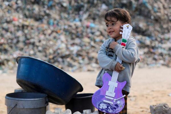 A displaced Palestinian boy holds a toy guitar near a dump site where he shelters with his family, amid an Israeli military operation, in the central Gaza Strip.