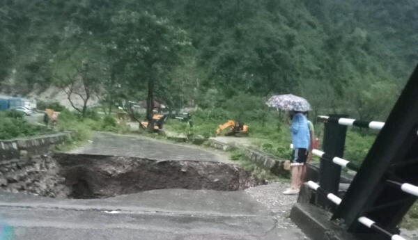 People look at a caved-in portion of a bridge after heavy rains triggered a cloudburst, near Maldevta in Dehradun.