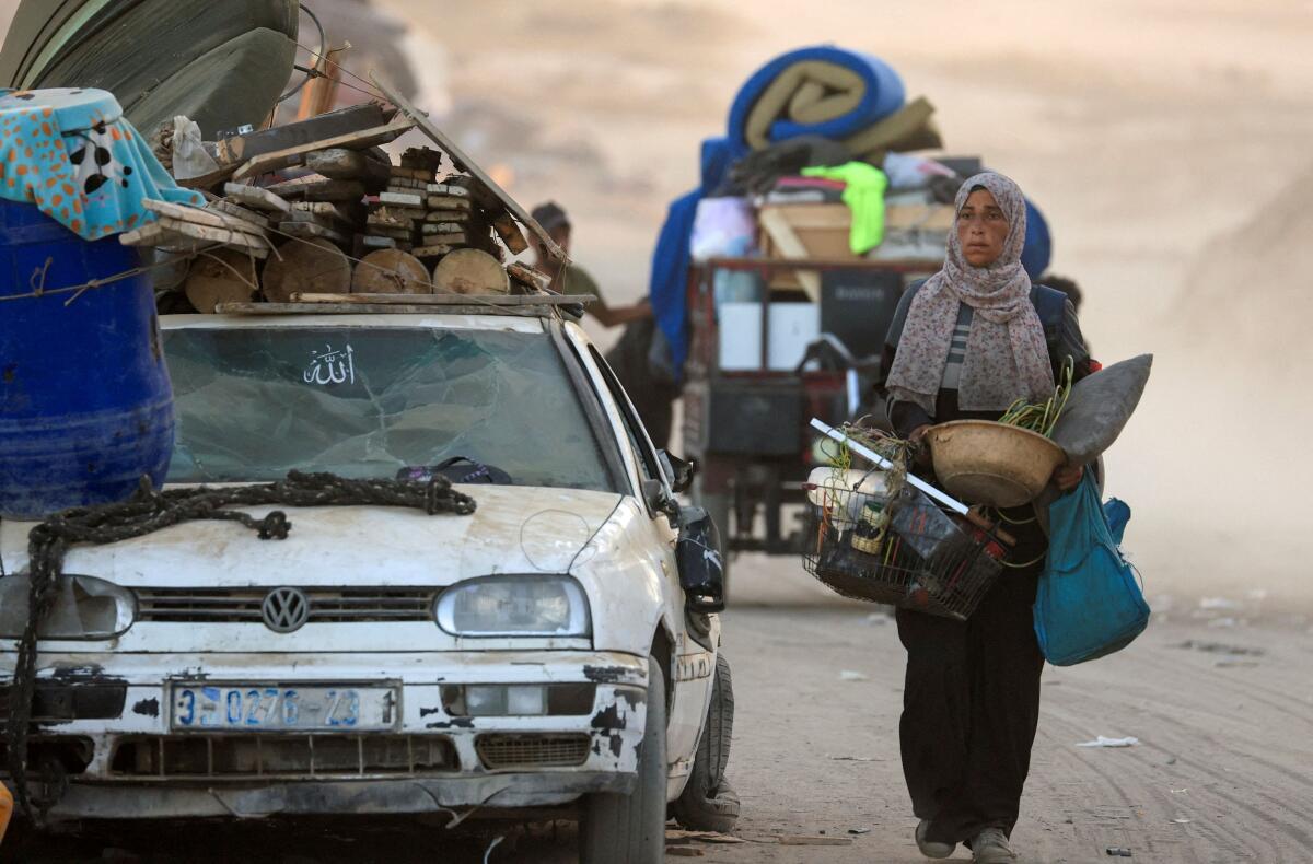 A displaced Palestinian woman, fleeing northern Gaza due to an Israeli military operation, carries belongings as she moves southwards after Israeli forces ordered residents of Gaza City to evacuate to the south, in the central Gaza Strip.
