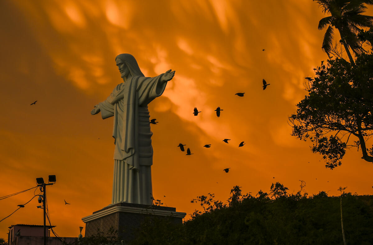 Birds fly by the statue of Christ The Redeemer during golden hour at the St. Joseph's Shrine, Vizhinjam, in Thiruvananthapuram, Kerala
