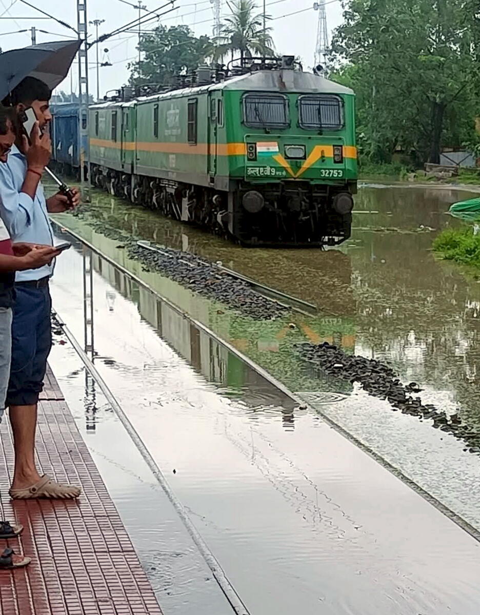 People stand at a platform while railway tracks lay submerged due to heavy rainfall, in Rohtas district, Bihar