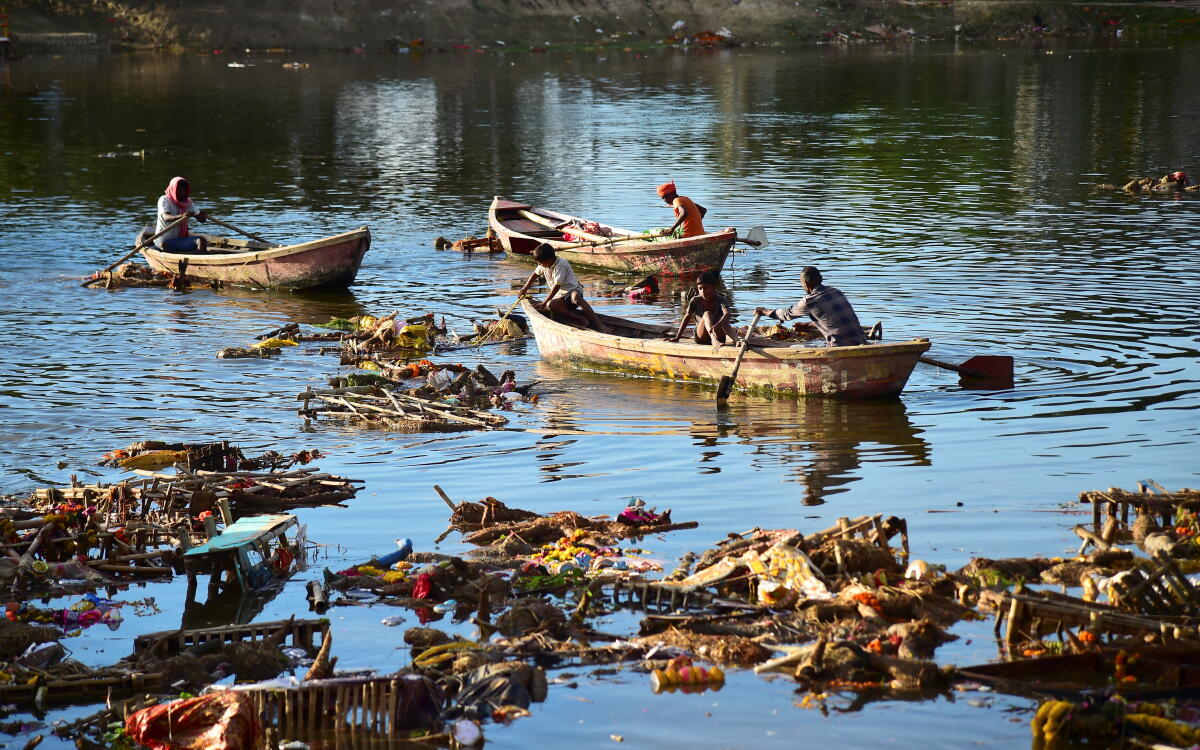 Boatmen look for coins and goods amid waste afloat in a pond following the immersion of idols of Goddess Durga after the 'Durga Puja' festival, in Prayagraj, Uttar Pradesh