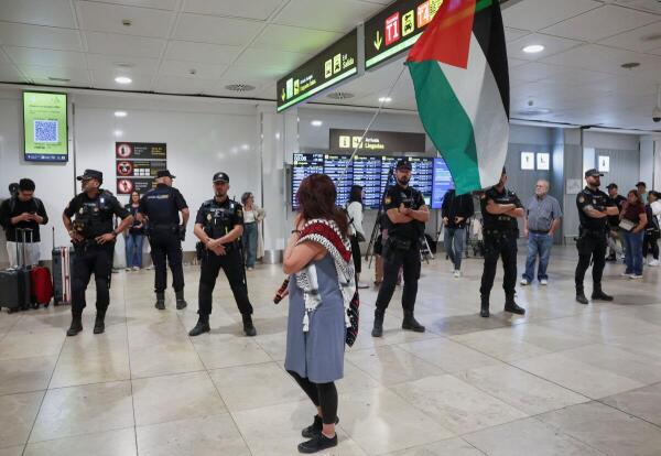 Police officers stand guard and a woman holds a Palestinian flag as Spanish activists and politicians who were part of Gaza humanitarian aid flotilla and were detained by Israeli forces arrive at Adolfo Suarez Madrid-Barajas Airport in Madrid, Spain.