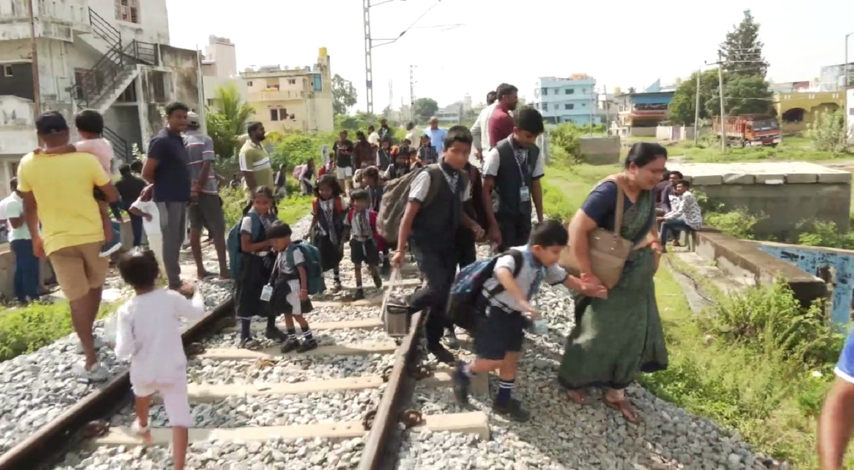 Parents help their kids to cross the railway track after the overnight rain flooded the underpass at Khadripur in Kolar, on Friday. DH PHOTO