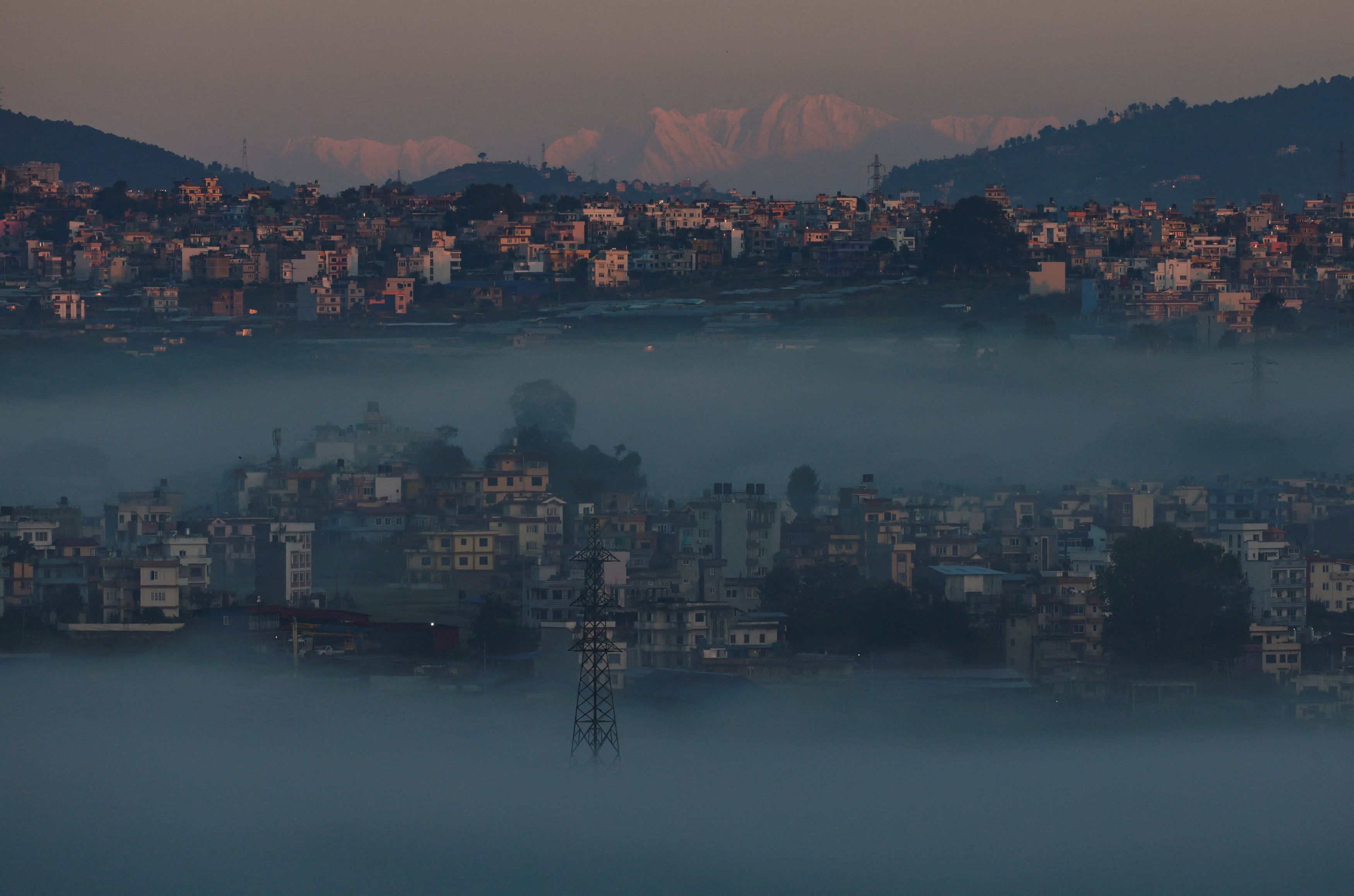 A snowcapped mountain range emerges over the valley during a foggy morning in Katmandu