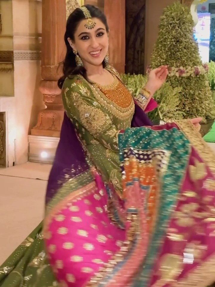 Channel regal vibes this festive season with Sara Ali Khan’s olive-green anarkali set, featuring exquisite gold zari, thread, and bead embroidery. Paired with a pink flared skirt, a colorful patchwork dupatta, chandbali jhumkas, and a bold maang tika, this look radiates royal grace.