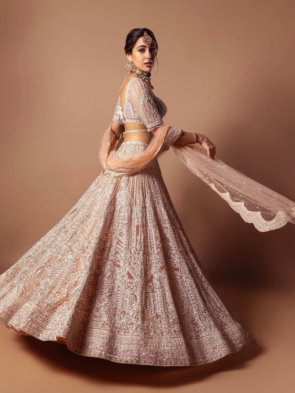 Steal the show this Diwali, just like Sara, in a gorgeous pink sequin lehenga set. The blouse with a sweetheart neckline, detailed silver embroidery, mirror accents, and pearl-drop tassels radiates royal elegance. Paired with a gleaming gota patti skirt, a scalloped dupatta and a striking choker, this look is all about festive luxury.