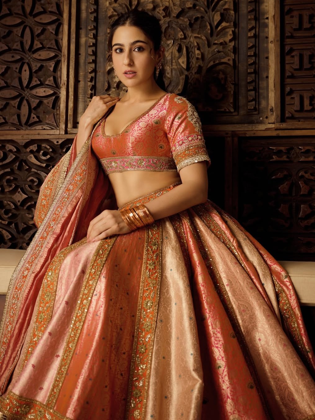 To steal the spotlight this Diwali, look no further than Sara Ali Khan’s peach-orange lehenga, adorned with detailed embroidery and golden borders. Styled with a deep-neck blouse, delicate earrings, a polished ponytail, and nude makeup, she exudes an effortlessly chic festive aura.