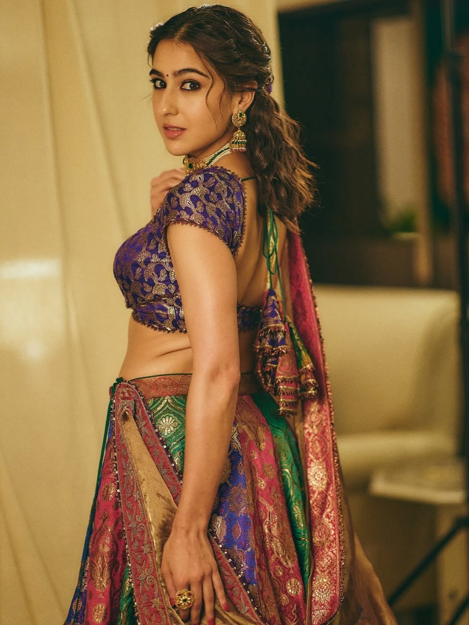 Embrace timeless elegance like Sara in a lehenga made from vintage brocade sarees. This striking ensemble includes a purple backless blouse with dori ties and gota patti accents, paired with a vibrant multi-colored brocade lehenga and a soft tissue silk dupatta.
