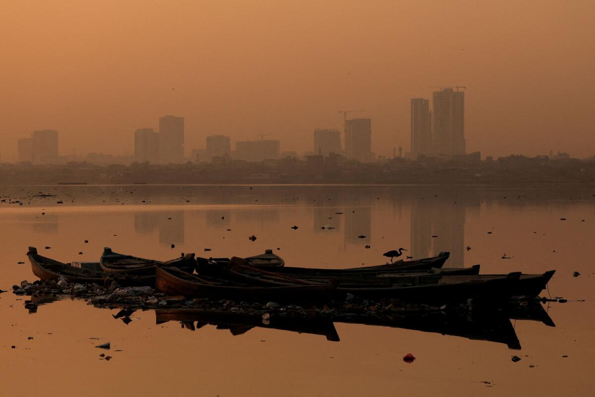 A bird sits on an anchored fishing boat, with buildings in the background amid smog and air pollution, in the morning, in Karachi, Pakistan.