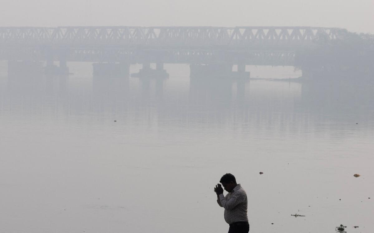 A man prays on the banks of the Yamuna river on a smoggy morning in New Delhi, India