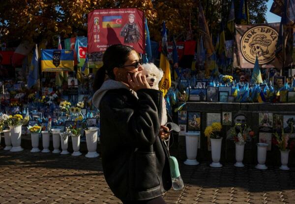 A woman with a dog walks near a makeshift memorial with the names of fallen service members written on Ukrainian and other national flags, at the Independence Square, amid Russia's attack on Ukraine, in Kyiv, Ukraine.